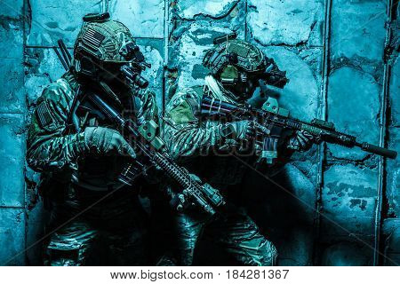 Squad of Army Rangers moving along the concrete wall on mission. They are ready to contact with enemy and to kill. Outdoor location shot, darkness of night, dim light