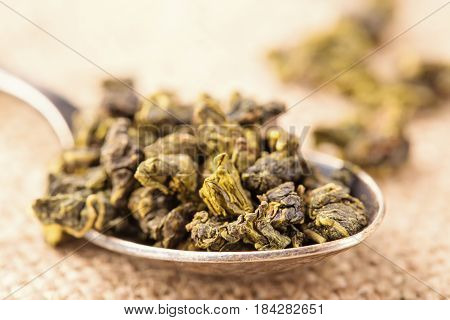 Dry leaves of green tea and teaspoon. A light background from fabric a close up selective focus. Grade milk oolong tea