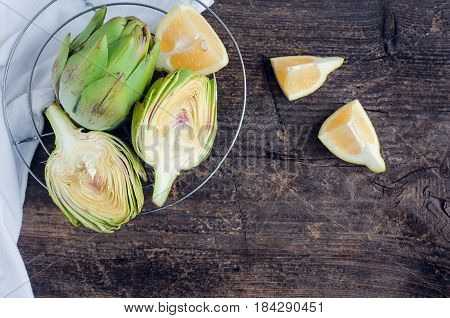 Two ripe fresh organic artichokes with lemon and white napkin on rustic wooden background with place for text. Top view. Copy space.