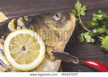 Mirror carp river fish with lemon herbs and pepper on dark wooden table.