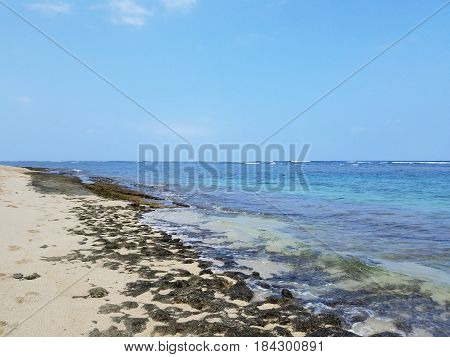 Rocky beach with Shallow wavy ocean waters of Camp Mokuleia Beach looking into the pacific ocean with a clear blue sky on Oahu.