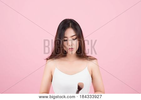 Beauty Asian Girl tan skin with Makeup Brushes. She smiling and looking to powder brush Natural makeup with beautiful v-shape face and long hair style.