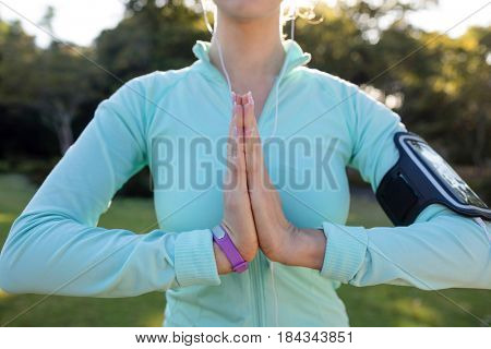 Mid section of female jogger listening to music and exercising with hands joint in the park