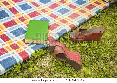 A book on a mat and high heels on the grass outdoor cropped shot concept of a weekend