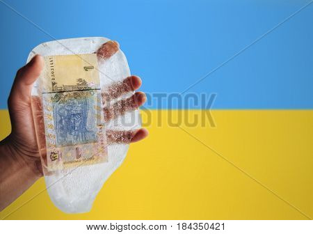 Ukrainian money in ice on a flag background. Devaluation, financial crisis, poverty.