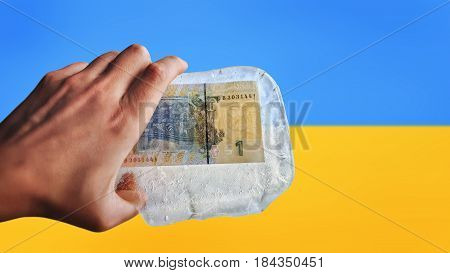Ukrainian money in ice on a flag background. Devaluation, financial crisis.