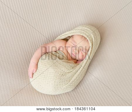 Adorable kid napping wrapped with a scarf, arm hanging out of it, sleeping tight