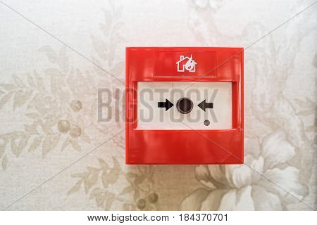 Closeup of red fire alarm box with black button on beige wall background