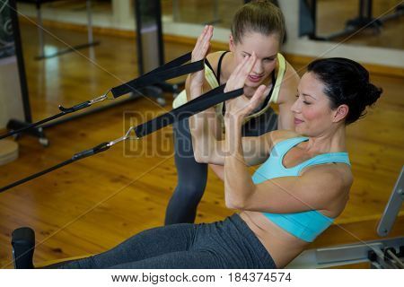 Female trainer assisting woman with stretching exercise in gym