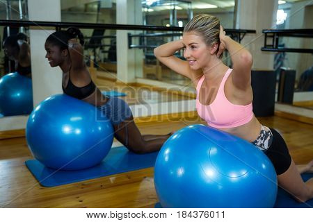Two smiling women performing pilate on exercise ball in fitness studio