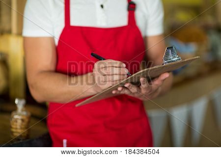 Mid section of bakery staff writing on clipboard at counter in bake shop