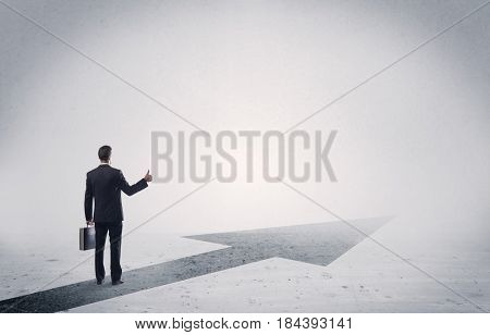 A professional businessman thinking while standing on a black arrow pointing forward in grey space concept