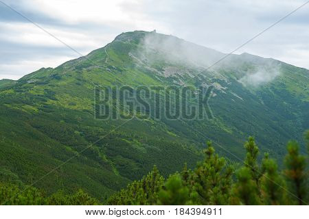 Magic mountain landscape. Ridge covered by a coniferous forest with mountain observatory on top misty morning.