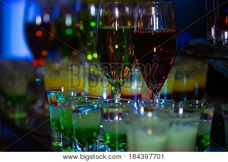 set of cocktails soft and long drinks on blurred background glasses with alcoholic layered shots mixed multicolored drink served in rows on countertop in bar or night club on blurred background