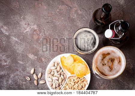 Beer in bottles and glasses closeup on the concrete table. Beer and snacks are pistachio nuts chips and nachos top view. Copy space. Drink and snack for the football match or rest in bub