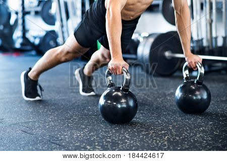 Unrecognizable young fit man doing strength training, doing push ups on kettlebells in modern gym.