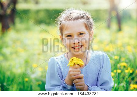 beautiful blue-eyed and blond girl in a meadow holding a dandelion in the hands