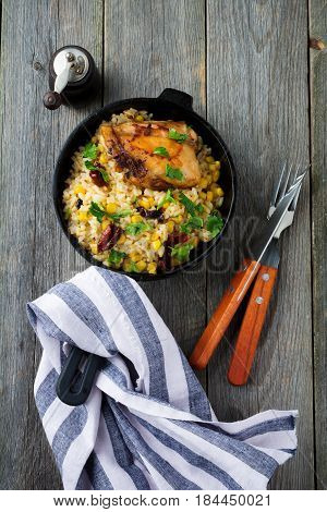 Rice with corn soy sauce and fried chicken thigh on a cast-iron frying pan. Top view. Selective focus.