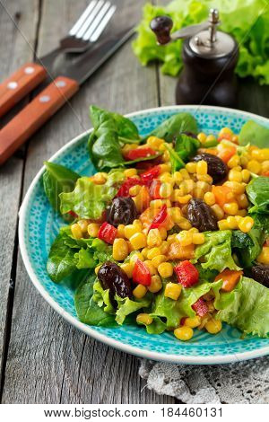 A warm salad with corn pepper olives and lettuce on a blue ceramic plate on a dark background. Selective focus.