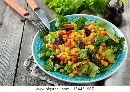 A warm salad with corn pepper olives and lettuce on a blue ceramic plate on a dark background. Selective focus.