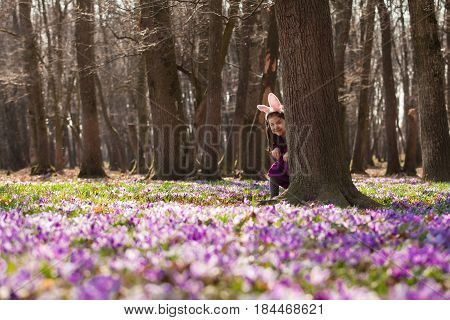 Little girl with banny ears peeping from behind a tree in the park