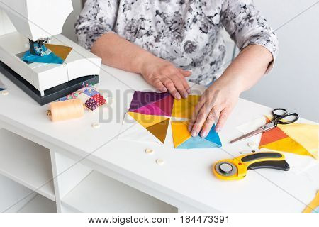 needlework and quilting in the workshop of a woman tailor - hands of tailor women put on the desktop the pieces of colored fabric, lay next to the scissors, buttons, pins, threads, rotary cutters