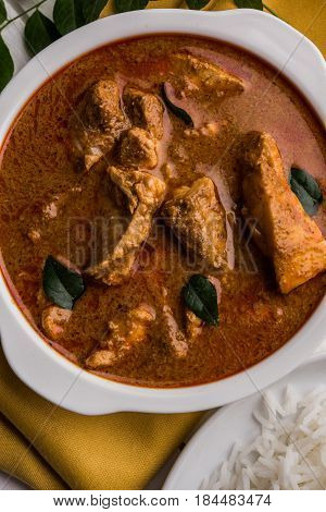 tasty fish curry served with white cooked basmati rice with curry leaves in the background, favourite coastal indian food