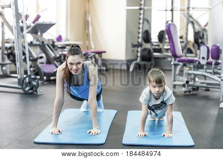 mother and son in sport shirts are doing plank in gym.