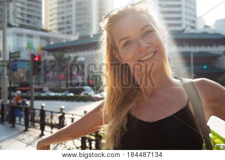 Attractive blond woman smiling and looking at the camera outdoors against scyscrapers background on sunny summer day