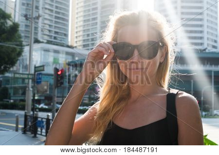 Attractive blond woman smiling and looking at the camera outdoors against scyscrapers background on sunny summer day