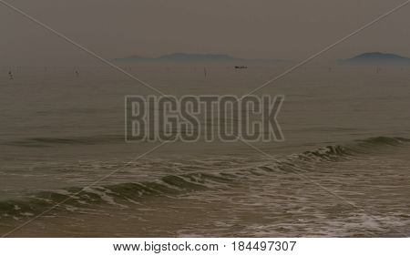 Seascape of Pacific ocean coast of Korea with islands hidden behind mist and fog and waves coming into shore.