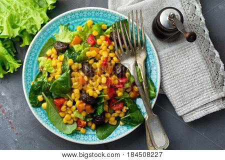 Warm salad with corn pepper olives and lettuce on a blue ceramic plate on a dark background. Selective focus.Top view.