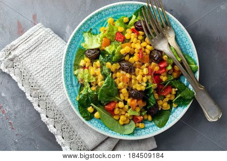 Warm salad with corn pepper olives and lettuce on a blue ceramic plate on a dark background. Selective focus.Top view.