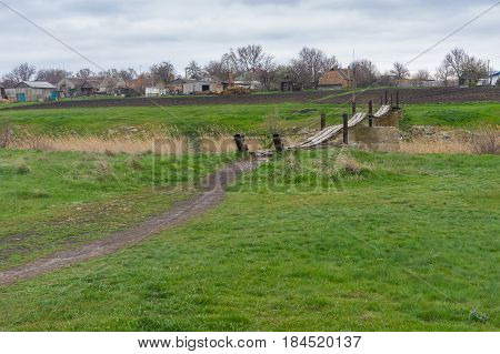 Spring landscape with meadow and old foot-bridge over small river Tomakivka in Topyla village central Ukraine