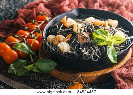 Black spaghetti with prawns and scallop in frying pan on black background