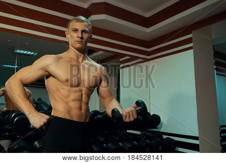 Beautiful strong man with a dumbbell in gym