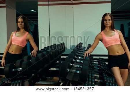 Beautiful girl standing near a dumbbell in the gym.