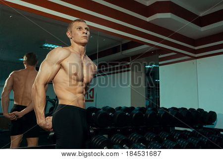 Beautiful bodybuilder near a dumbbell in the gym.