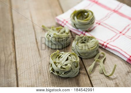 Roll of raw tagliatelle pasta and napkin on wooden surface