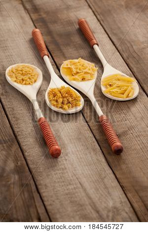 Spoons filled with varieties of pasta on wooden background