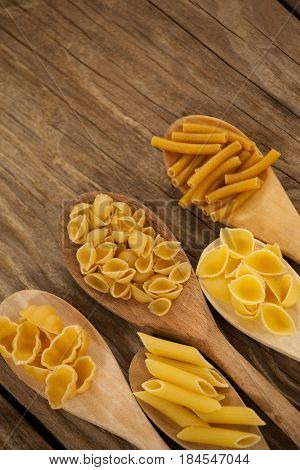 Spoons filled with varieties of pasta on wooden background