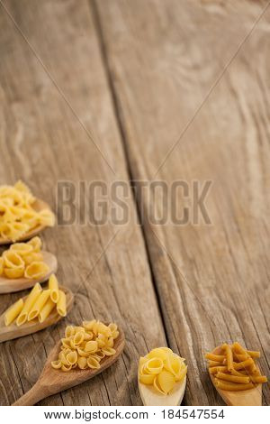 Spoons filled with varieties of pasta on wooden background