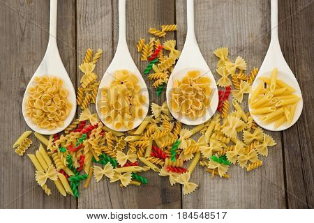 Spoons filled with varieties of pasta on wood surface