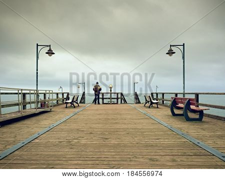 Man On Wooden Mole In Harbor Within Autumn Misty Day. Tourist At Handrail.