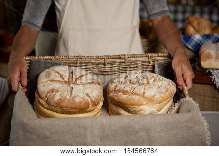 Mid-section of female staff holding wicker basket of breads at counter in bakery shop