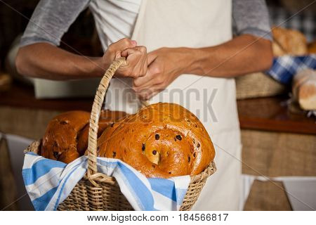 Mid-section of female staff holding wicker basket of breads at counter in bakery shop