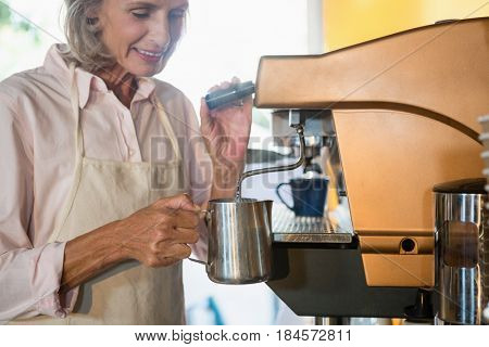 Senior waitress using coffeemaker in cafe