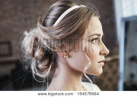 Beauty photo of young woman with knot of hair and professional makeup. Side view.