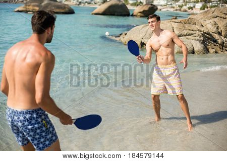 Shirtless male friends playing matkot on shore at beach