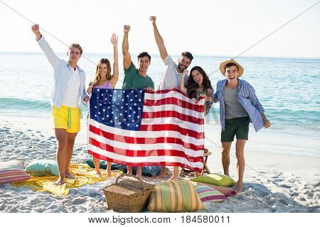 Happy friends holding American flag while standing on shore at beach